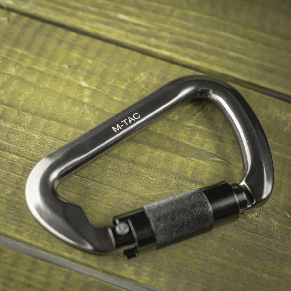 M-Tac Key-Lock Karabinhage i aluminium på træoverflade, ideel til klatring og sikkerhed, CE EN362 certificeret, ergonomisk design.