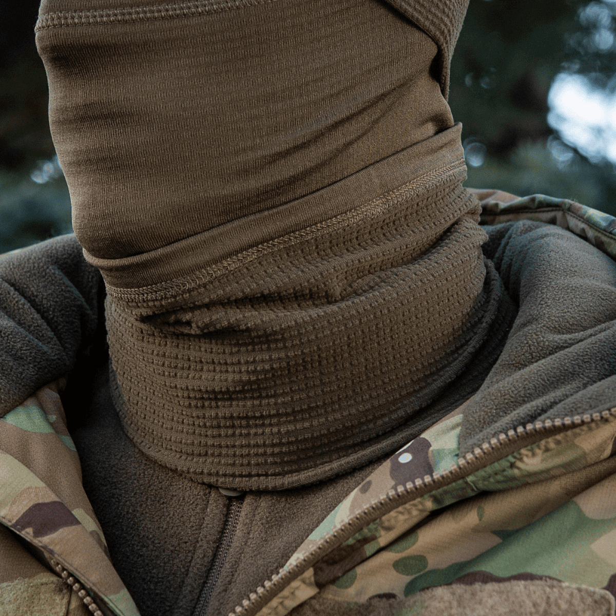 Person iført M-Tac Tube Scarf Polartec Power Grid i tåget skov, designet til varme og beskyttelse af ansigt og hals mod kulde.