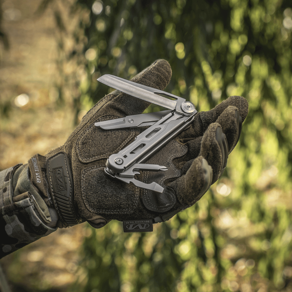 Alt Tag: M-Tac Type 3 Foldekniv (5-i-1) Rustfrit Stål multiværktøj holdt i hånd iført camouflagehandske i naturen