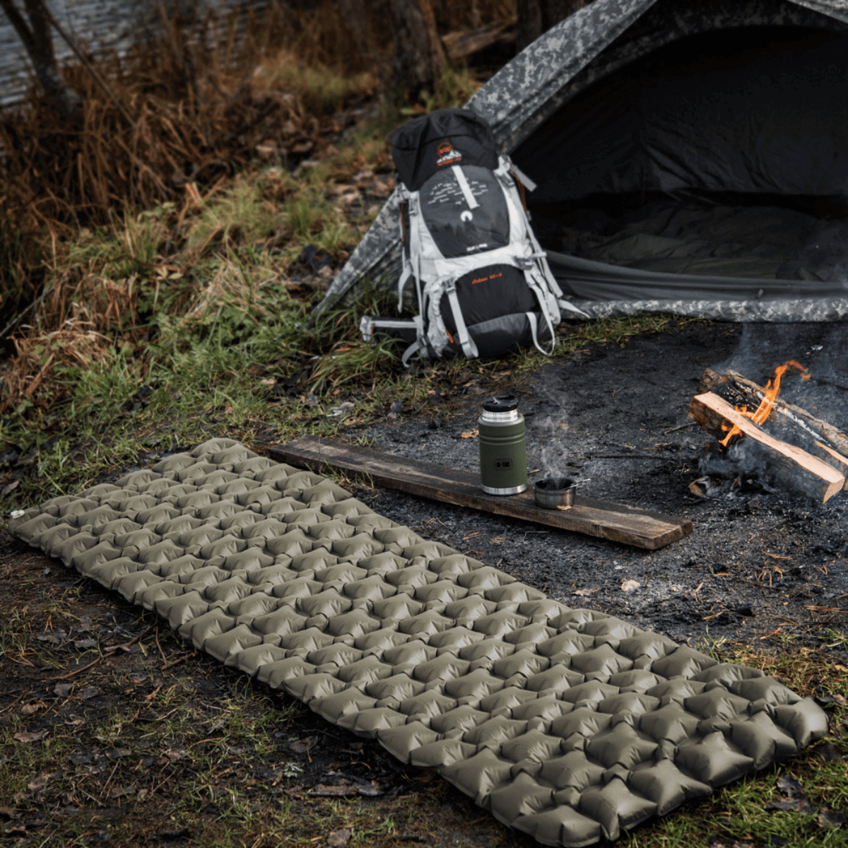 M-Tac Oppustelig Liggeunderlag 195x60 ved siden af telt i skov, ideelt til camping og beskyttelse mod varmetab på kolde overflader