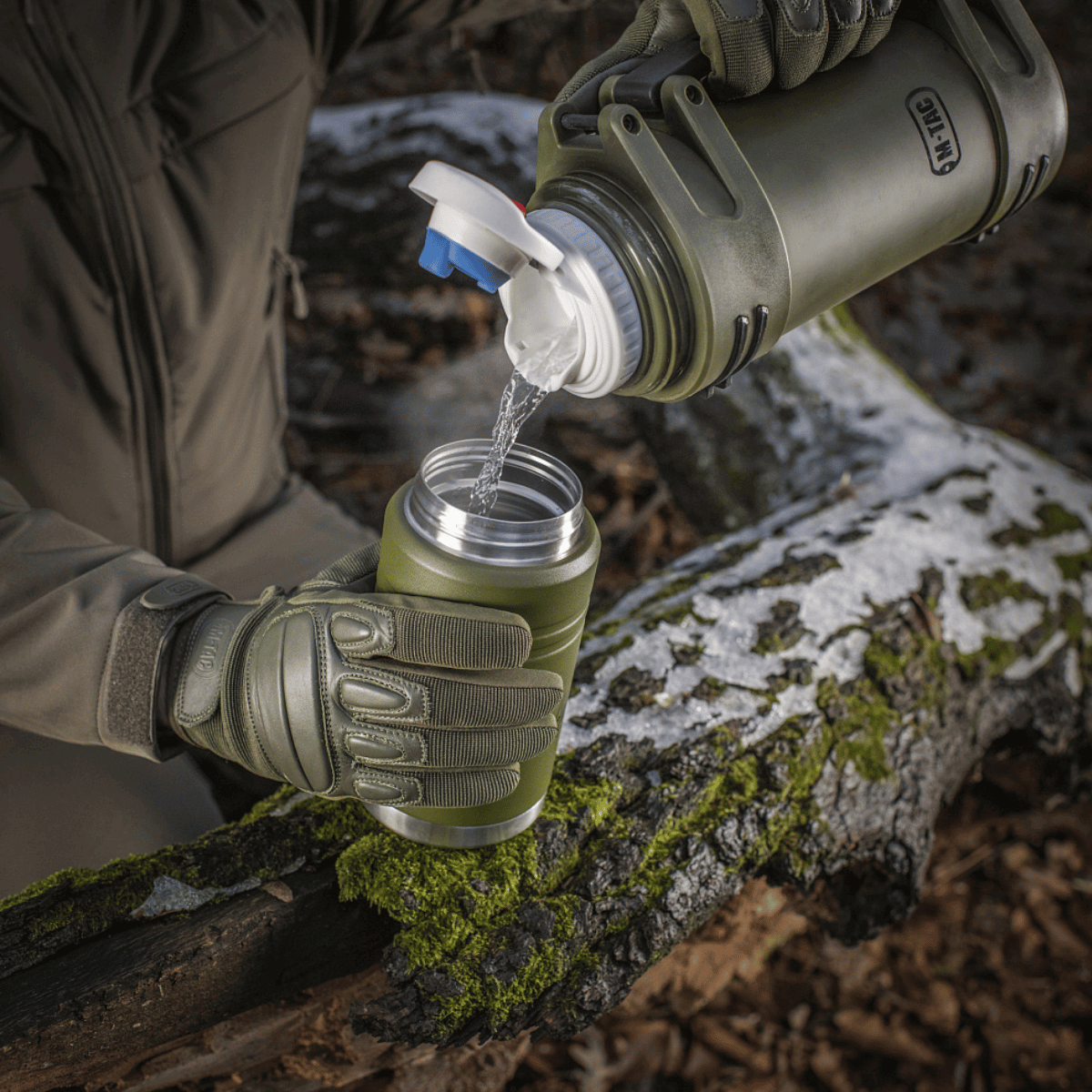 Person hælder vand fra en grøn M-Tac Termoflaske 750 ml med Folde-ske ude i naturen