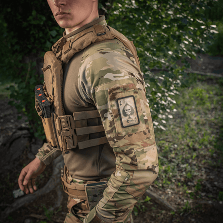 Man in camouflage with M-Tac Patch Ace of Spades on the arm in a natural environment.