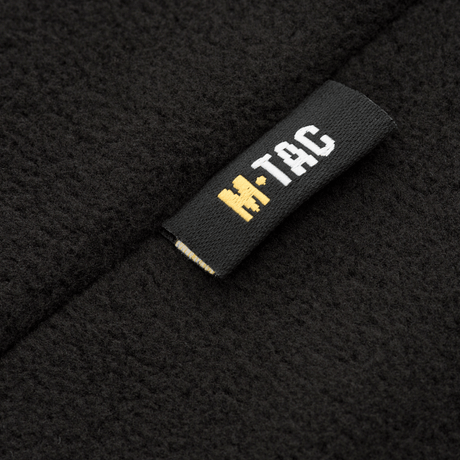 Nærbillede af M-Tac Delta Fleece Jakke etikette, sort og gul logo, fleece materiale, ideel til udendørs og kolde vejrforhold