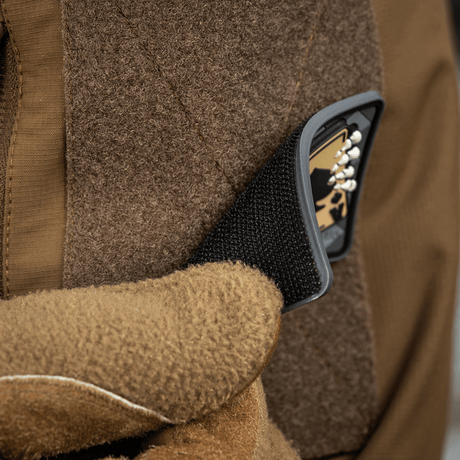 Brown gloved hand attaches M-Tac Joker Skull 3D PVC patch to jacket with Velcro.