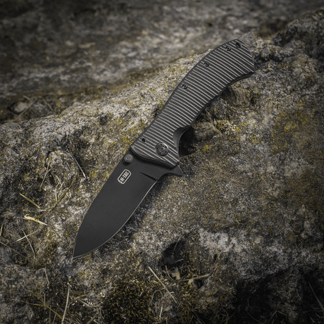 M-Tac Outdoor & Military folding knife - Type 7 on a rock surface, lightweight design with black‑coated 5Cr15MoV blade and frame-lock.
