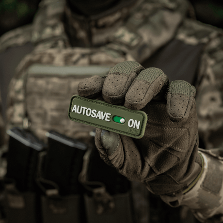 Tactical operator holding M-Tac Patch Autosave PVC 3D morale patch with Velcro, suitable for clothing or gear.