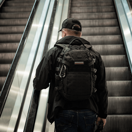 M-Tac Patch Flag 25x80 Mini Squares on a Cordura 500D backpack worn by a person on an escalator.