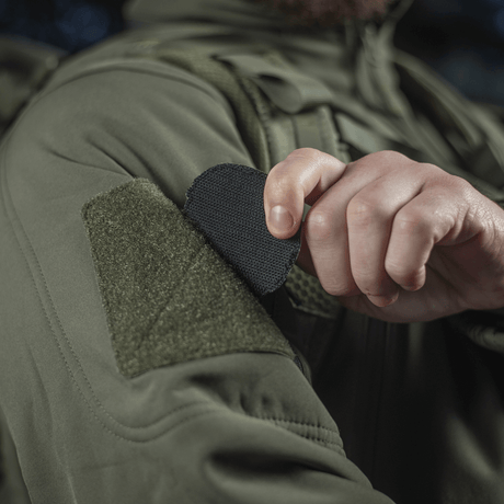 Person attaching M-Tac Patch Operator 3D PVC with Velcro to a jacket, tactical design morale patch, 6x7 cm, made of PVC.