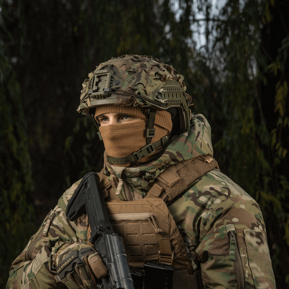 Militærperson iført M-Tac Rip-Stop Fleece Hjelmliner og camouflagetøj i skovmiljø, ideel til koldt vejr.