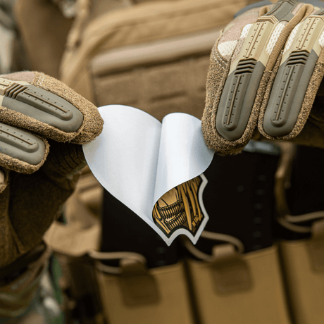 Person wearing tactical gloves holds a M-Tac Valkyrie sticker in front of a bag.