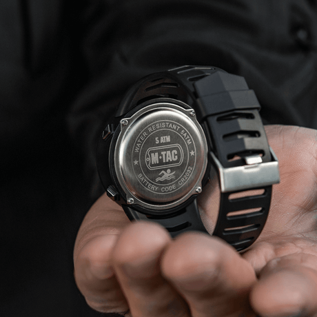 M-Tac Tactical Watch 2147 with steel back, "WATER RESISTANT 5ATM" and "BATTERY CODE CR2032" visible in a hand.