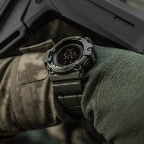 M-Tac Tactical Watch with Compass 2233 on a military-clad arm, exploration and outdoor adventure, rugged watch designed for tactical use with compass and LED display.