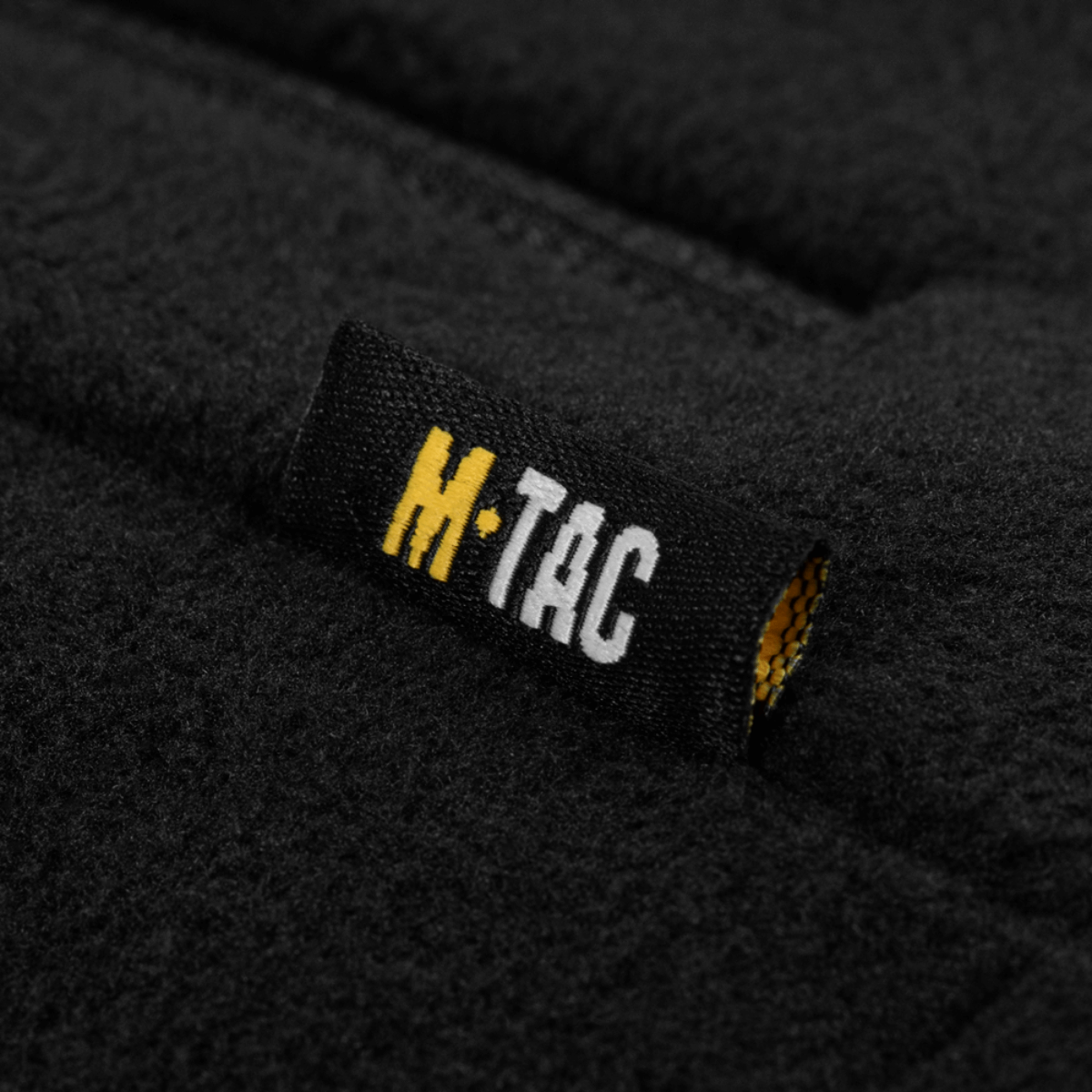 Label på M-Tac Combat Fleece Jakke Dame – Polartec og taktisk, viser mærkelogo på sort fleece materiale.