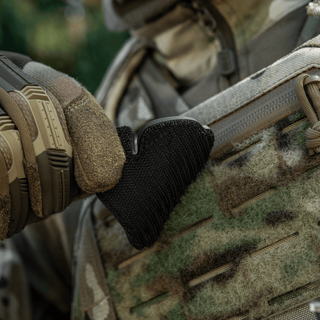 Tactical glove adjusts black velcro patch on camouflage clothing outdoors.
