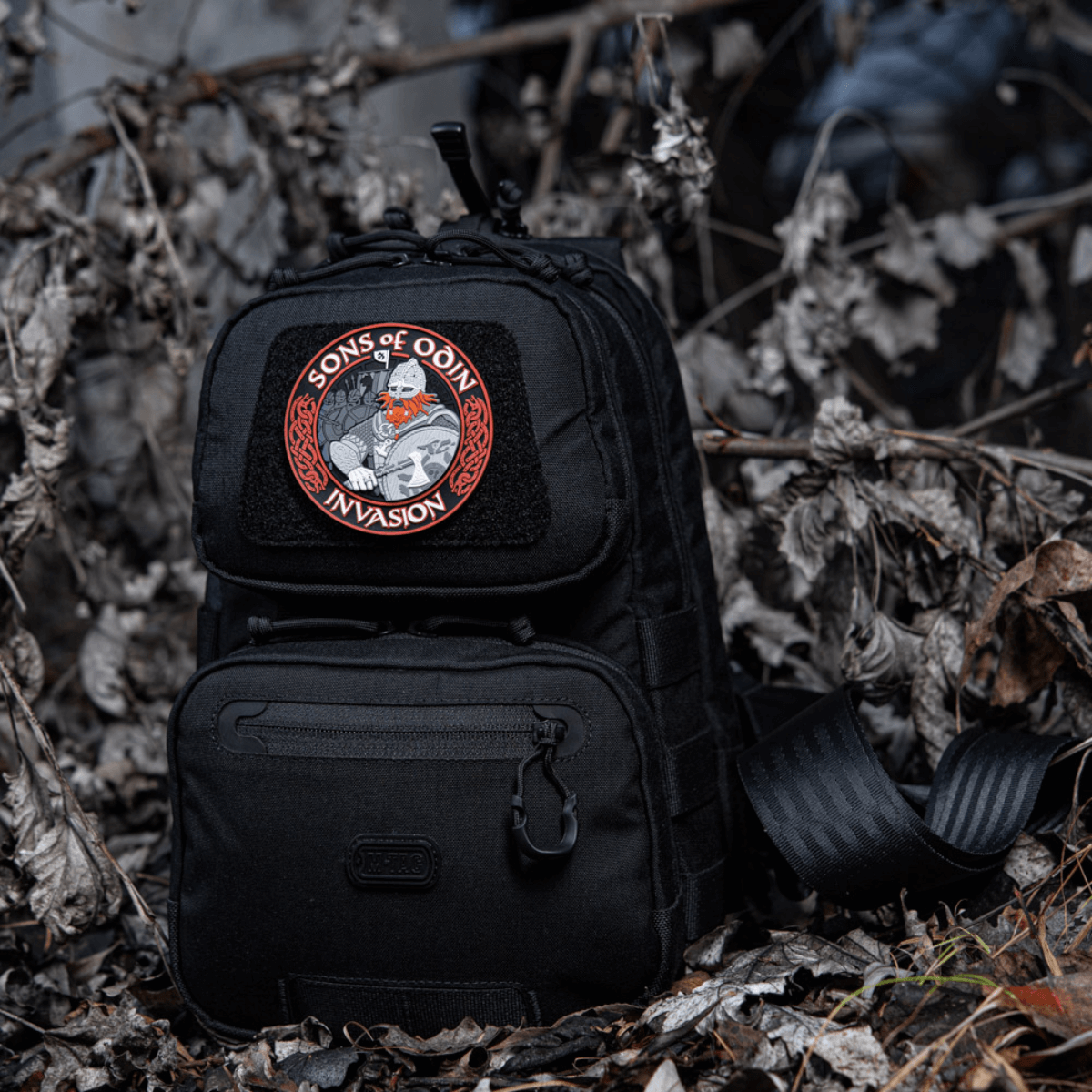 Sort rygsæk med M-Tac Patch Sons of Odin 3D Velcro i skovklædt område, velegnet til taktisk brug og fritid.