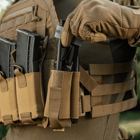 Person iført taktisk vest med M‑Tac Tourniquet Pouch Elastic Gen.5, Coyote Brown, til sikker opbevaring af CAT tourniquet.