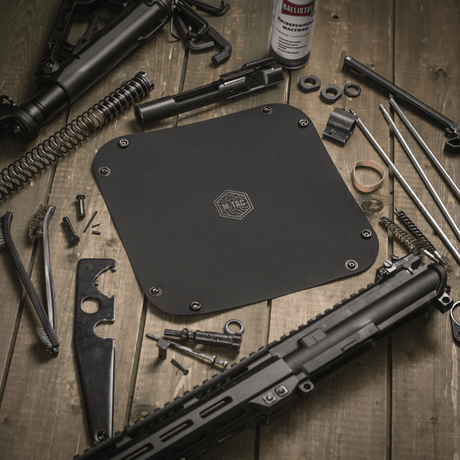 M‑Tac Maintenance Tray 24x24 cm with tools and firearm parts on a wooden table.