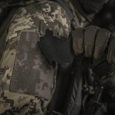 Soldier in camouflage jacket attaching M‑Tac Patch Baba-Yaga Vertical to a sleeve with Velcro.