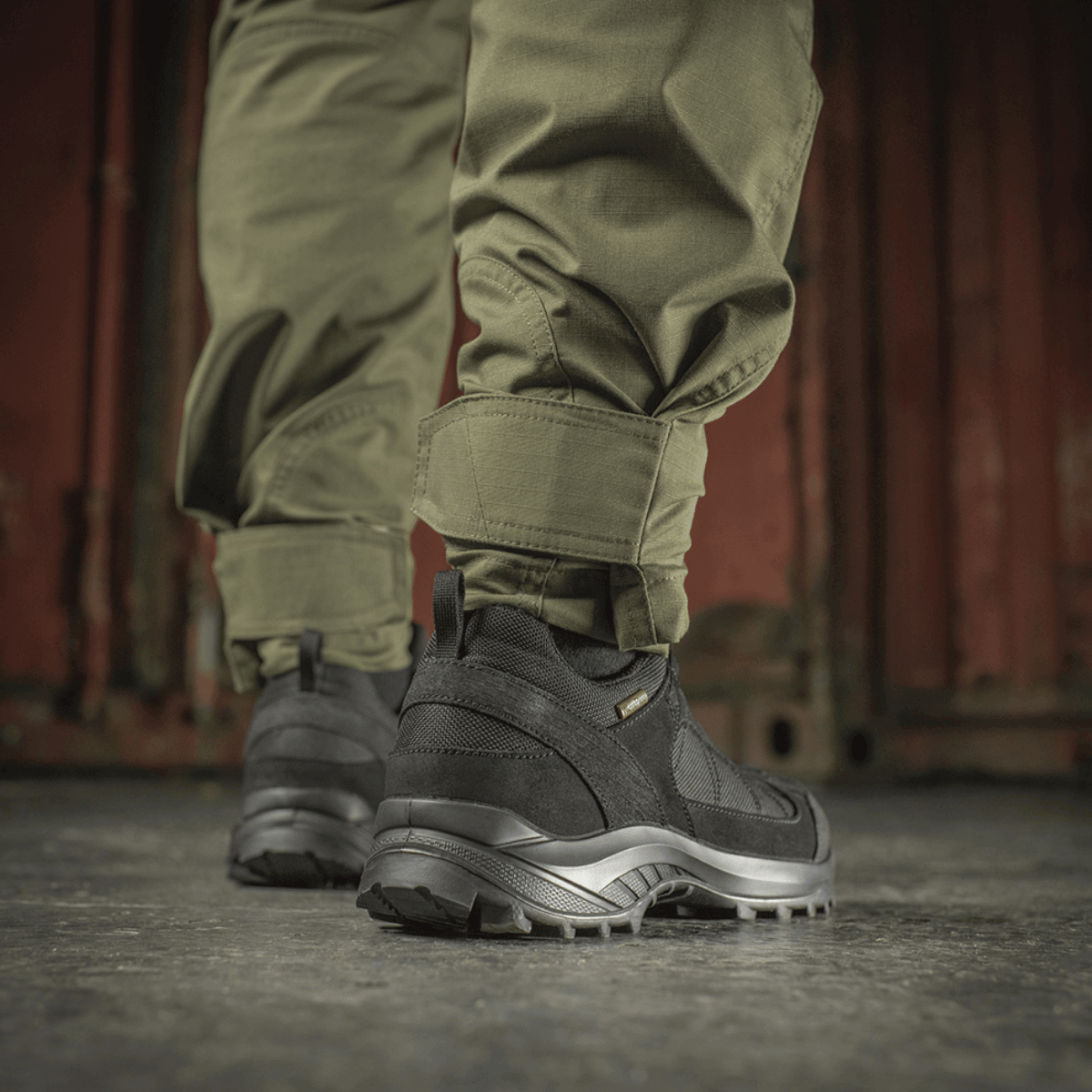 M-Tac Taktiske Bukser Aggressor Gen. II Flex i olivengrøn med robuste sorte støvler, velegnet til udendørsaktiviteter.