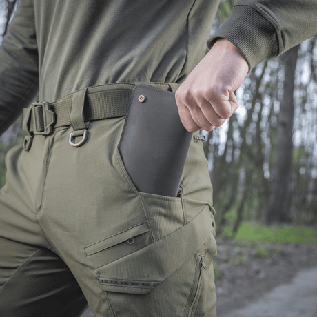 Person iført M-Tac Bukser Aggressor Summer Flex med telefon i lommen på udendørs sti.