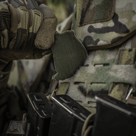 A soldier adjusts an M-Tac Jolly Roger PVC patch on his camouflage vest during outdoor tactical training.