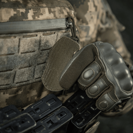 Soldier wearing tactical gear and gloves installs M-Tac Patch M67 Grenade 3D PVC with Velcro backing on camouflage uniform.
