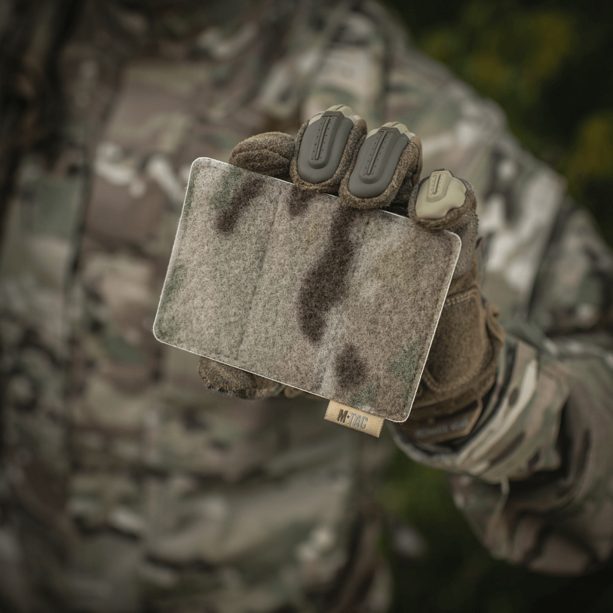 M-Tac Panel til Patches på MOLLE 120x85 i camouflageelement, holdt af person i taktisk udstyr, med hook & loop overflade.