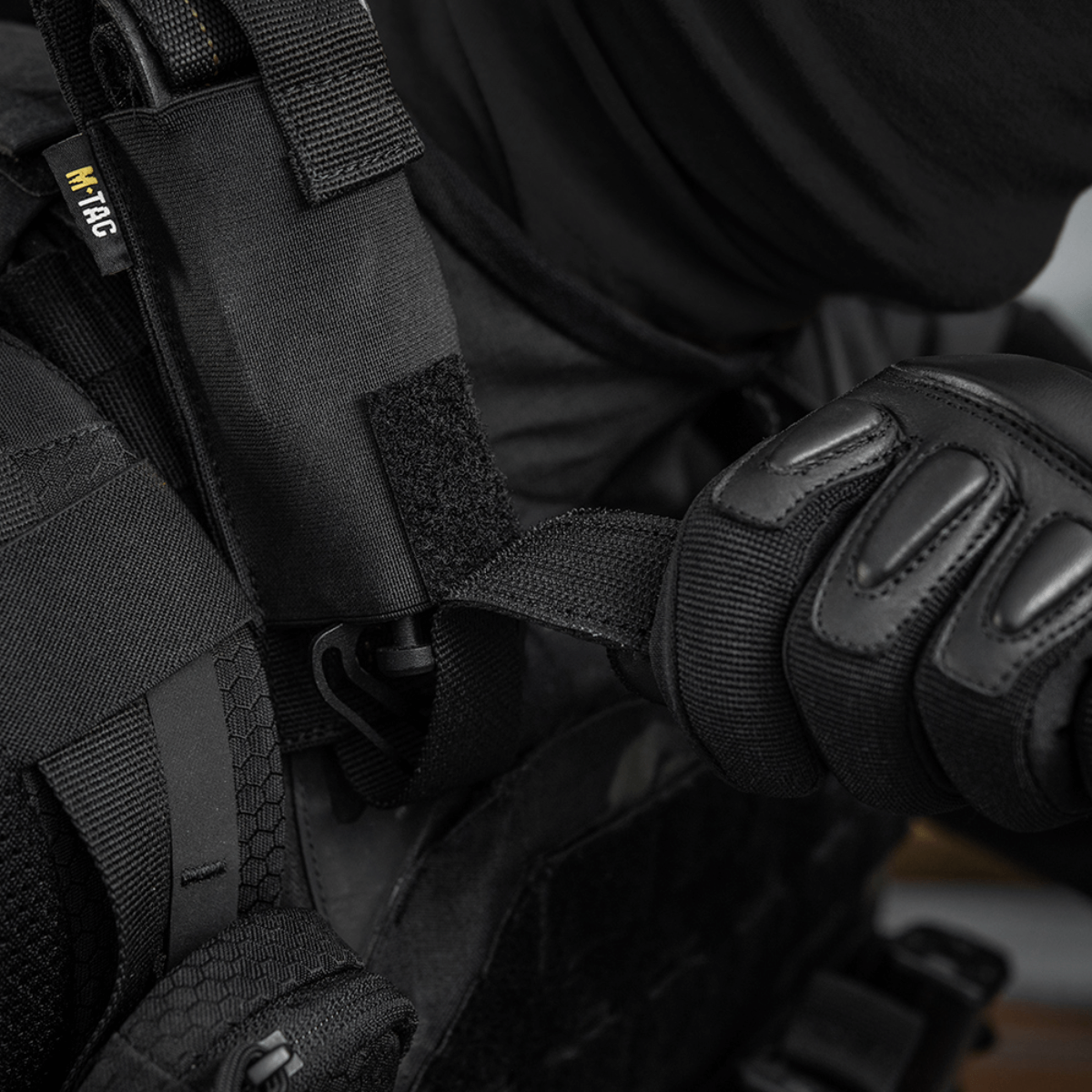 Person iført sort beskyttelsesudstyr bruger M-Tac Tourniquet Pouch Elastisk med MOLLE Gen.II fastgjort til vesten