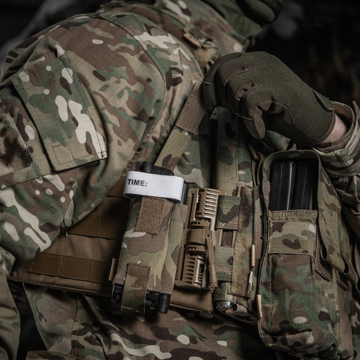 M-Tac Elastisk Tourniquet Pouch Molle Gen.III fastgjort til taktisk vest med tourniquet og ekstraudstyr i militær område.