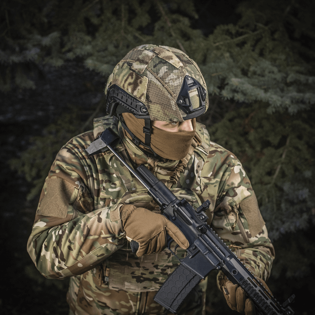 Person in camouflage gear wearing M‑Tac Hjelmcover Shroud Elite on helmet, holding a rifle in a forest environment.
