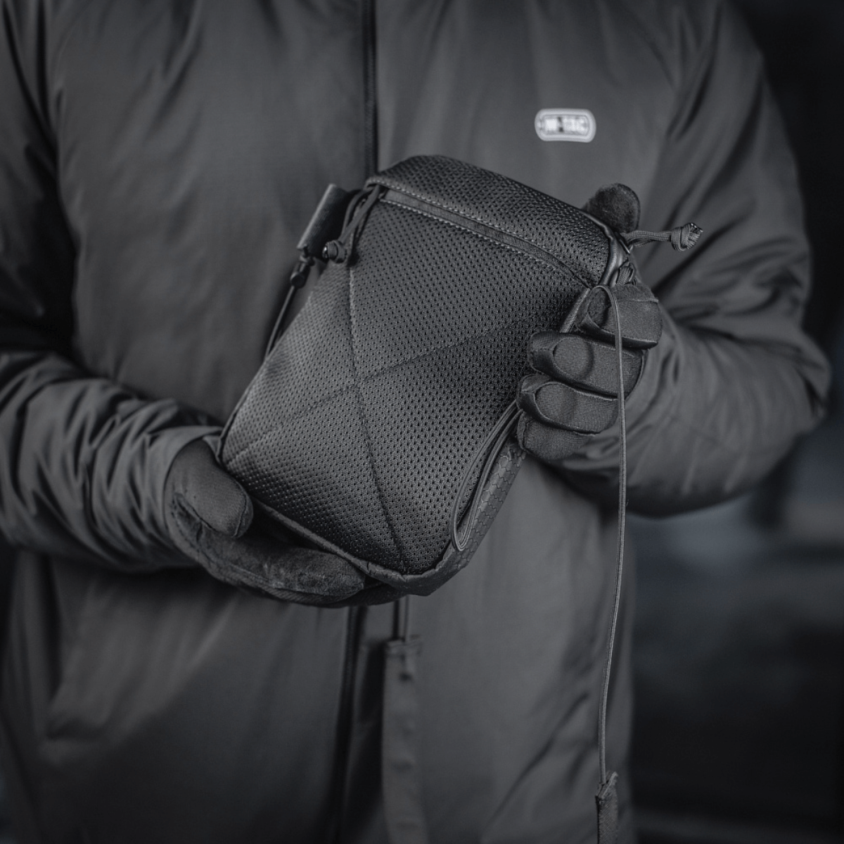 M‑Tac Pocket Bag Elite HEX i sort, holdt af en person med handsker. Kompakt taske perfekt til opbevaring af diverse småting.