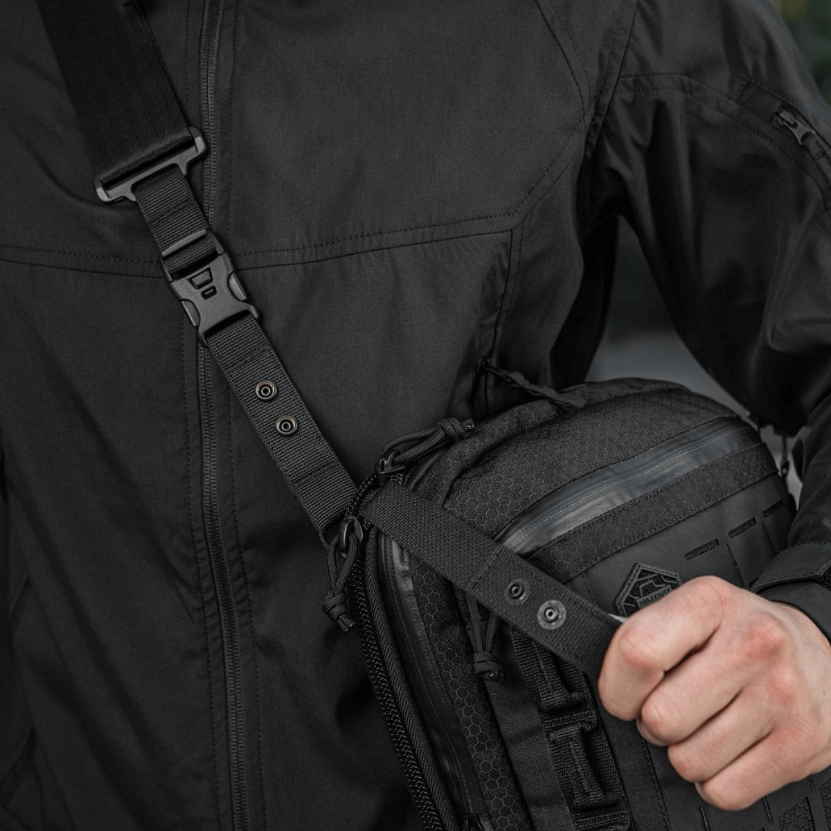 Person carrying M-Tac Tablet Bag Laser Cut Hex with shoulder strap and MOLLE panel in black.