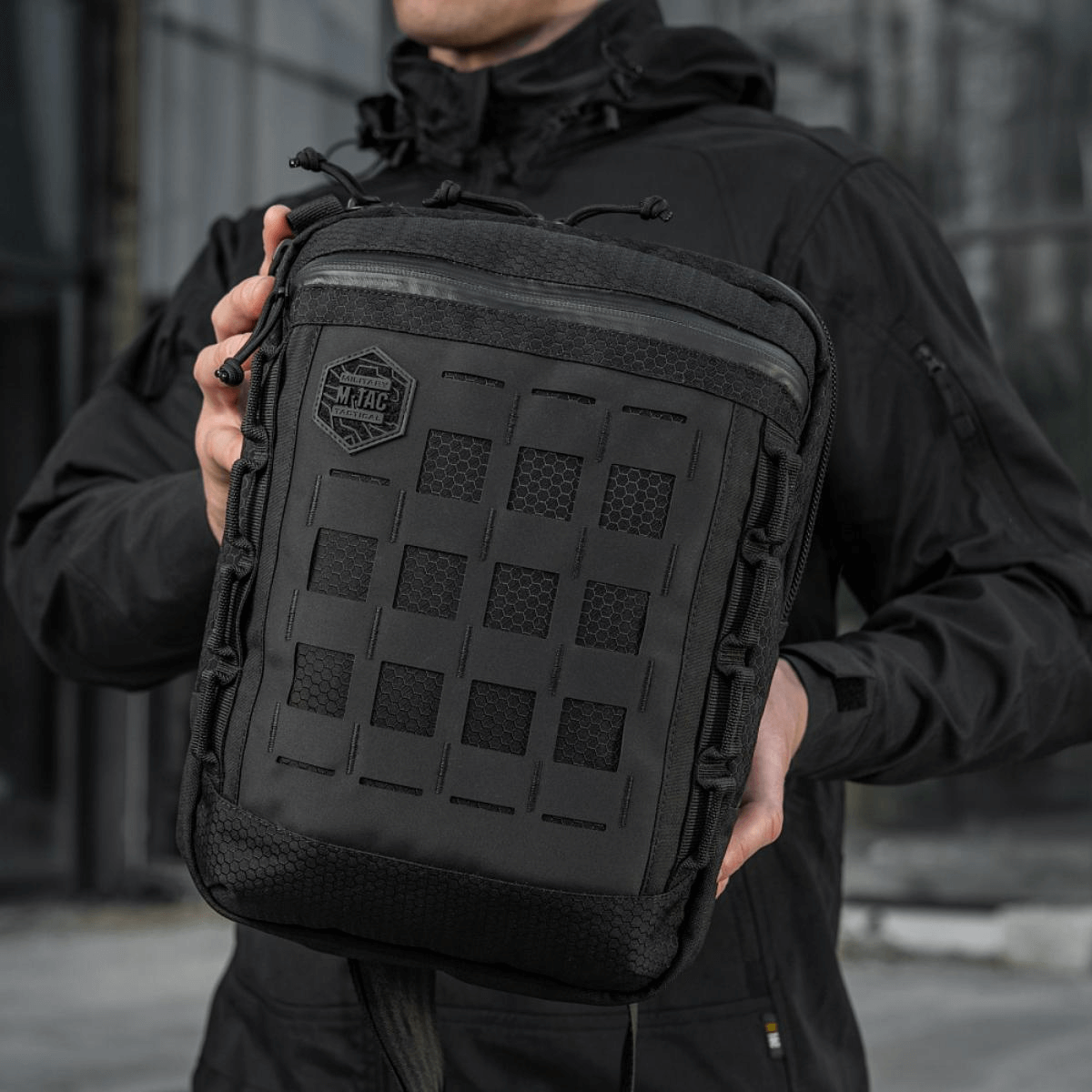 M-Tac Tablet Bag Laser Cut Hex i Cordura stof med Laser Cut MOLLE og hurtig adgang, holdt af en person i sort jakke.