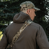 Person wearing a camo cap and jacket with a camouflage strap outdoors