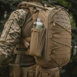 Taktisk militærrygsæk med vandflaske i sidelommen, set udendørs. Velegnet til udendørs aktiviteter og kampagner.