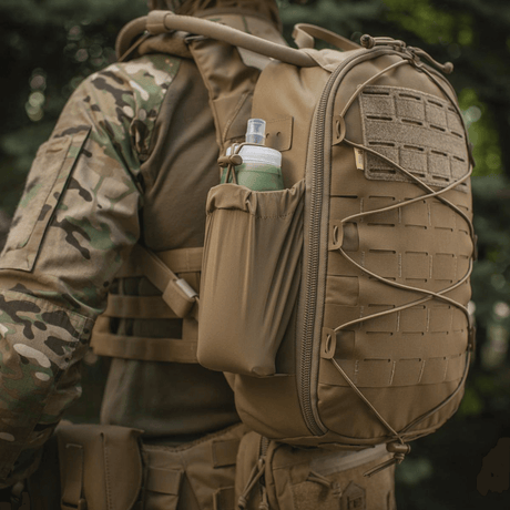 Taktisk militærrygsæk med vandflaske i sidelommen, set udendørs. Velegnet til udendørs aktiviteter og kampagner.