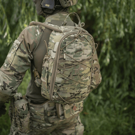 Soldat i camouflageuniform bærer taktisk rygsæk i skovområde