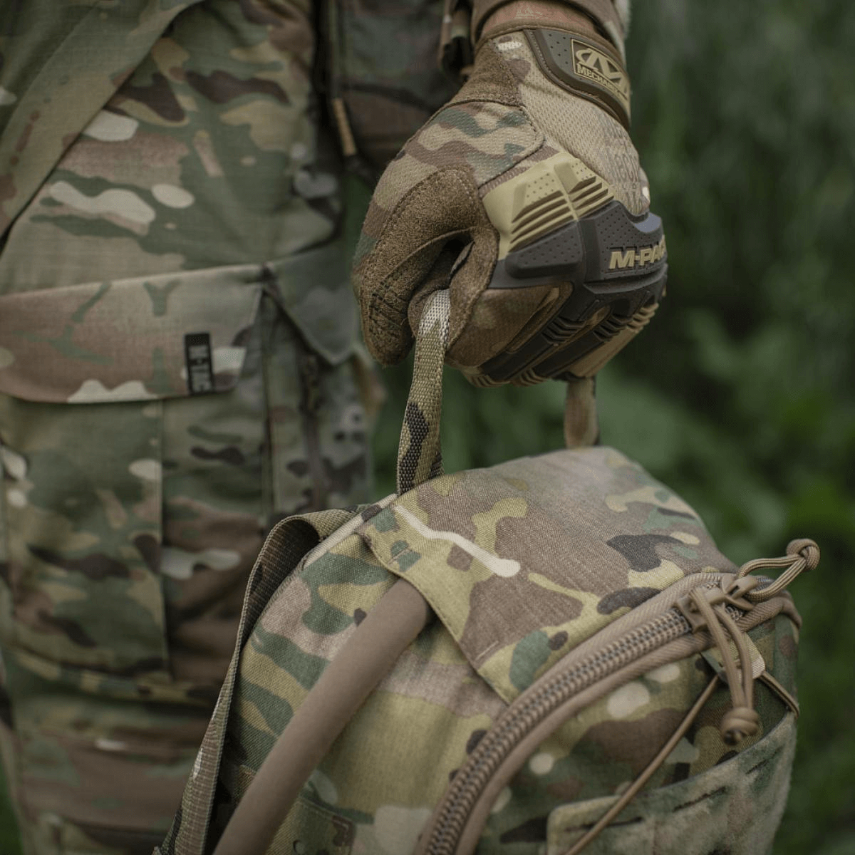 Militærperson i camouflageuniform med taktisk rygsæk, griber håndtag i skoven
