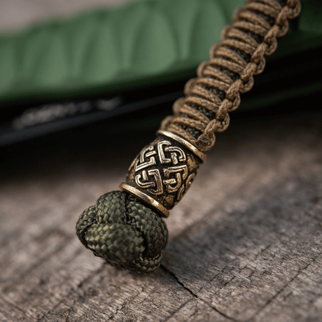 M-Tac Knife Lanyard Celtic i flettet paracord med keltisk mønster, knivtilbehør på trælignende overflade.