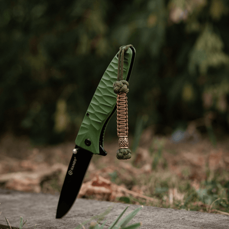 M-Tac Knife Lanyard Celtic - grøn foldekniv med flettet paracord lanyard i udendørs miljø.