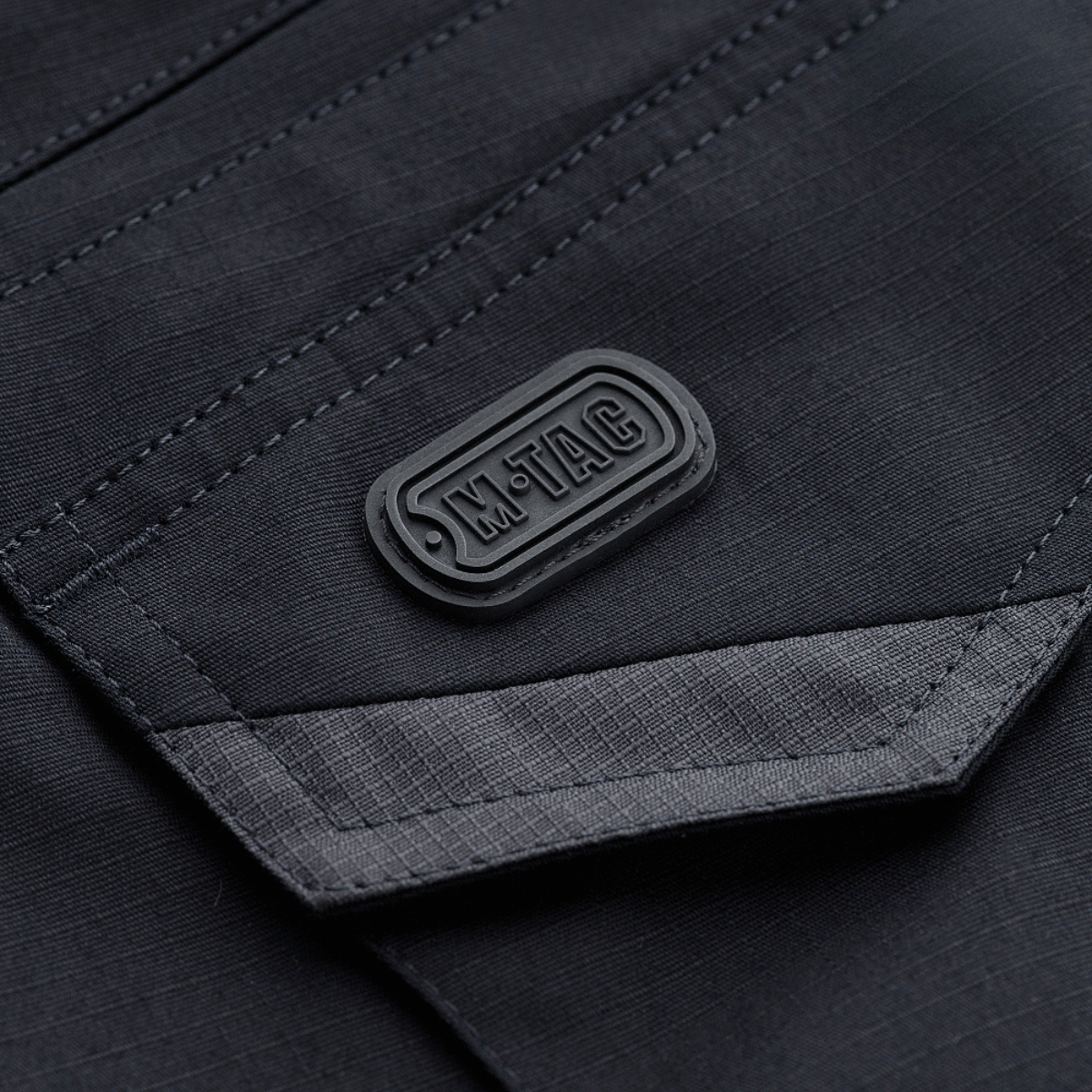 Detaljebillede af M-Tac Shorts Aggressor Gen.II Flex med M-Tac logo, lavet af rip-stop materiale med Teflon-belægning.