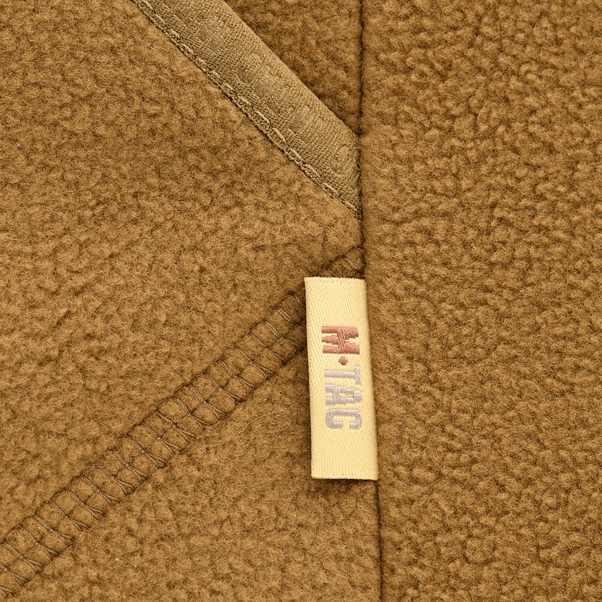 Nærbillede af M-Tac Lite Microfleece Hættetrøje i brun mikrofleece med M-Tac logo på sømmen, fokus på materiale og detalje.