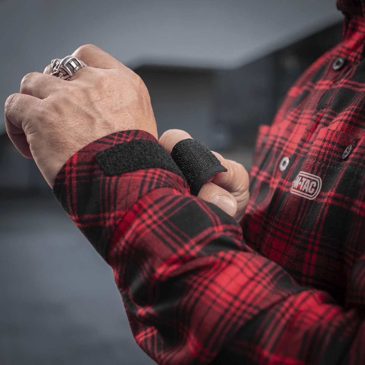 Person justerer velcrostrop på M-Tac Redneck Skjorte i taktisk plaid design.