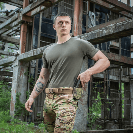 Mand iført M-Tac T-shirt 93/7 Summer ved en industriel bygning, perfekt til hverdagsbrug og sommerens varme dage.