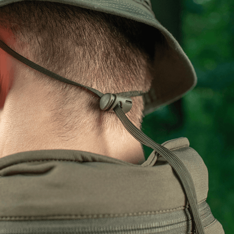 Viser bagsiden af en M-Tac Panama Rip-Stop hat, med justerbar snor for sikker pasform, set i naturmiljø.