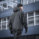 Mand bærer M-Tac Alpha Gen.III Pro Vinterjakke, perfekt til temperaturer ned til -20° C, foran moderne bygning.