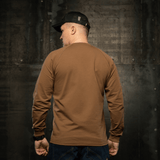 Mand iført M-Tac Raglan Athlete sweatshirt med raglanærmer i coyote-farve, set bagfra mod industriel baggrund.