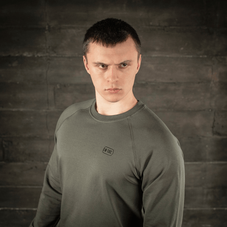 M-Tac Raglan Athlete sweatshirt i olivenfarve med raglanærmer, ideel til sport og hverdag, vises af en model mod betonbaggrund.