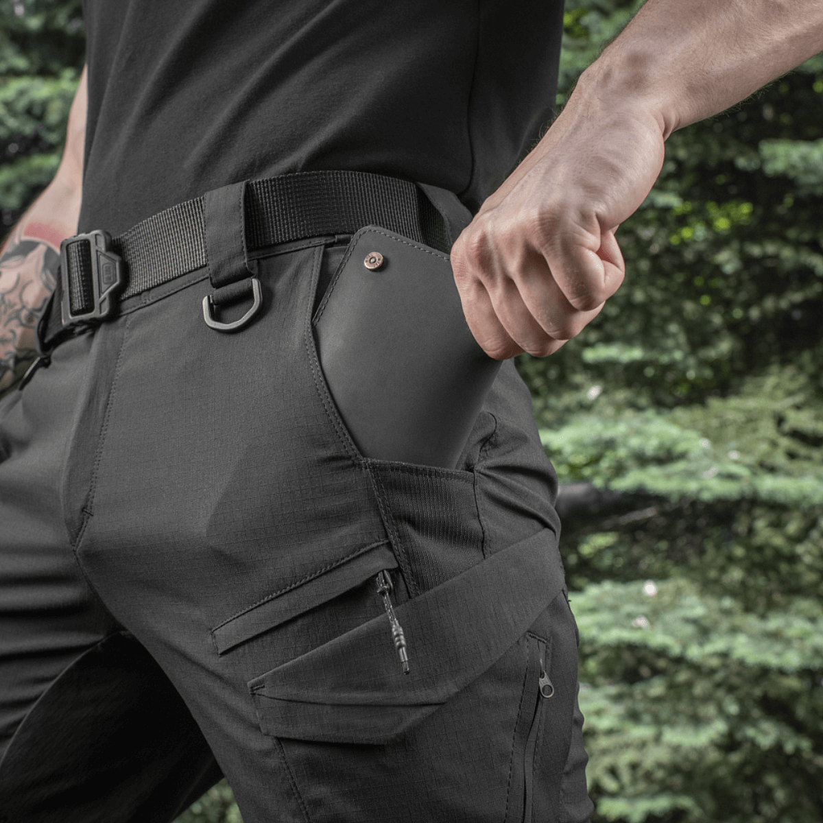 Mand iført M-Tac Aggressor Summer Flex Shorts med D-ringe, funktionelle lommer, perfekt til taktisk brug og udstyr, udendørs baggrund.