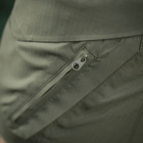 Nærbillede af lomme med lynlås på M-Tac Aggressor Summer Flex Shorts i grøn rip-stop stof.